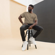 Load image into Gallery viewer, Man sitting on a stool wearing a SUCCESS WIRE Brown Savana color t-shirt with SUCCESS WIRE logo, black pants, and white sneakers against a plain background.
