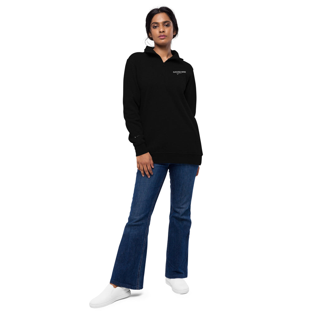 Woman wearing a SUCCESS WIRE black quarter zip pullover and blue jeans on a white background