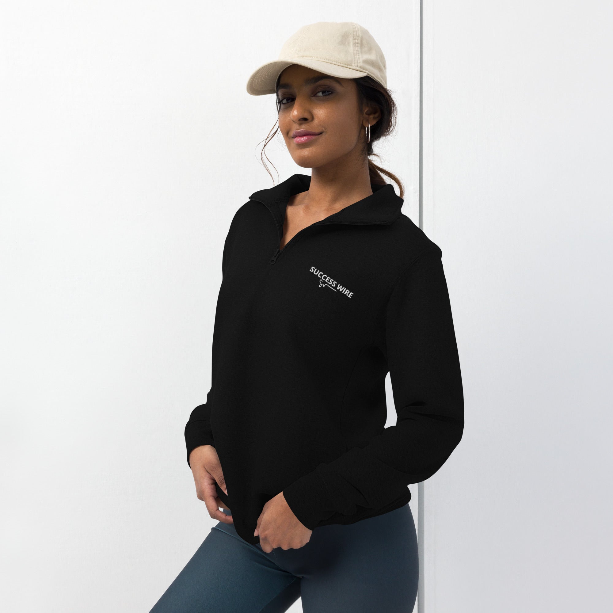 Woman wearing a black quarter zip with SUCCESS WIRE logo, standing against a white background