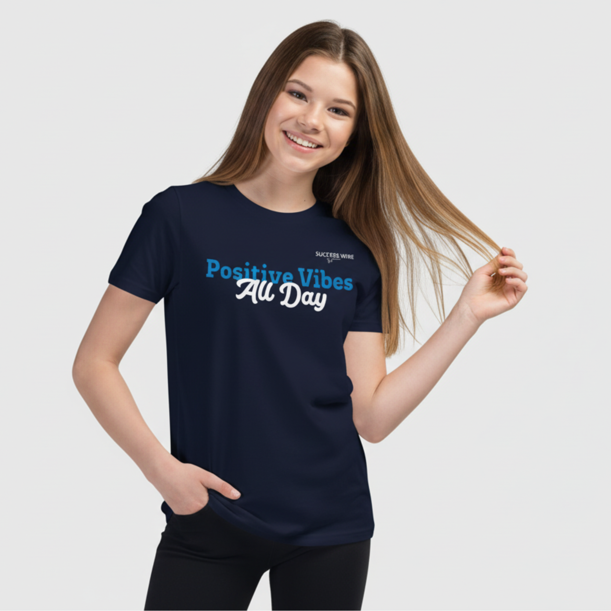 Young girl wearing a navy blue SUCCESS WIRE t-shirt with 'Positive Vibes All Day' text on a light gray background